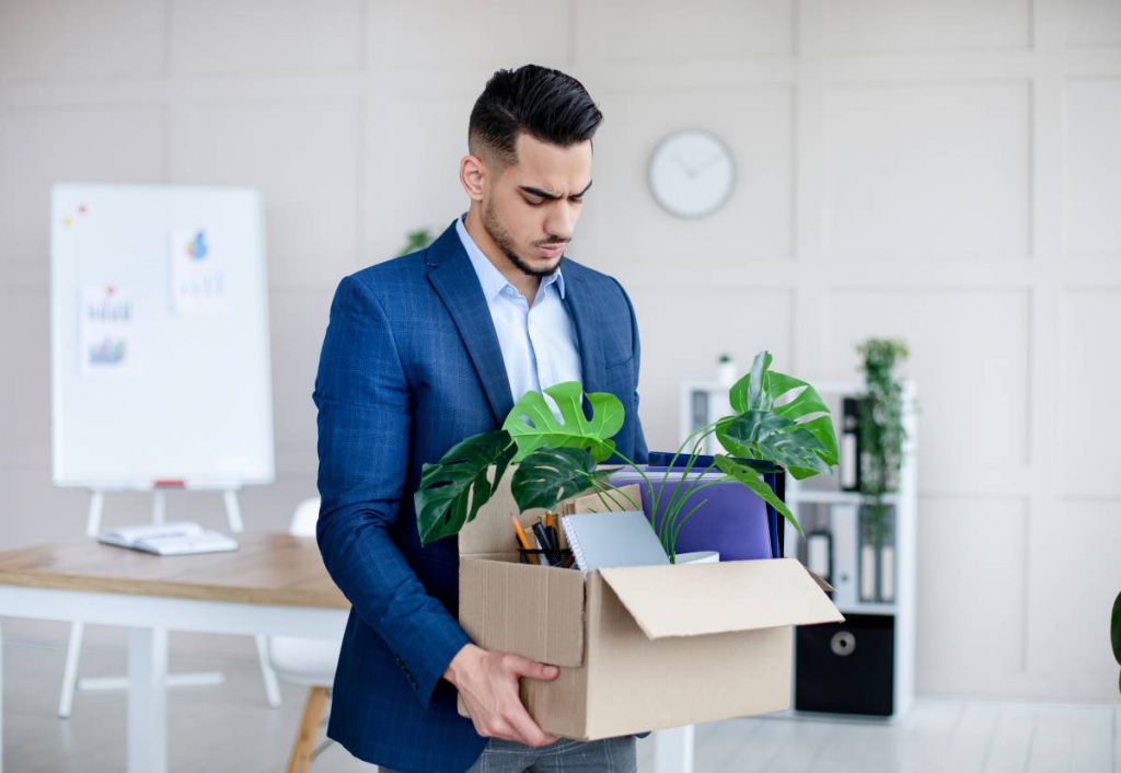 Un homme chômeur en costume tenant une boîte avec des plantes: L'allocation chômage est un revenu de remplacement en cas d’un licenciement d’un salarié non agricole.