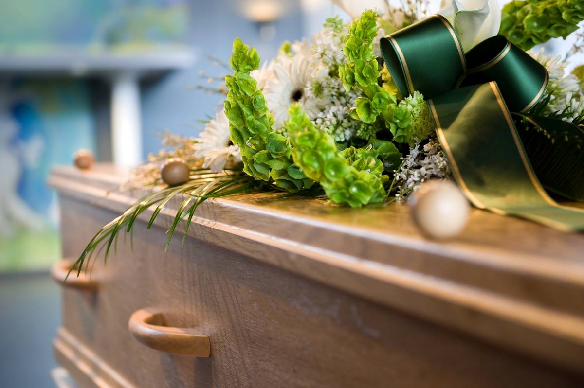 Un cercueil avec des fleurs et un ruban vert : Indemnité de décès